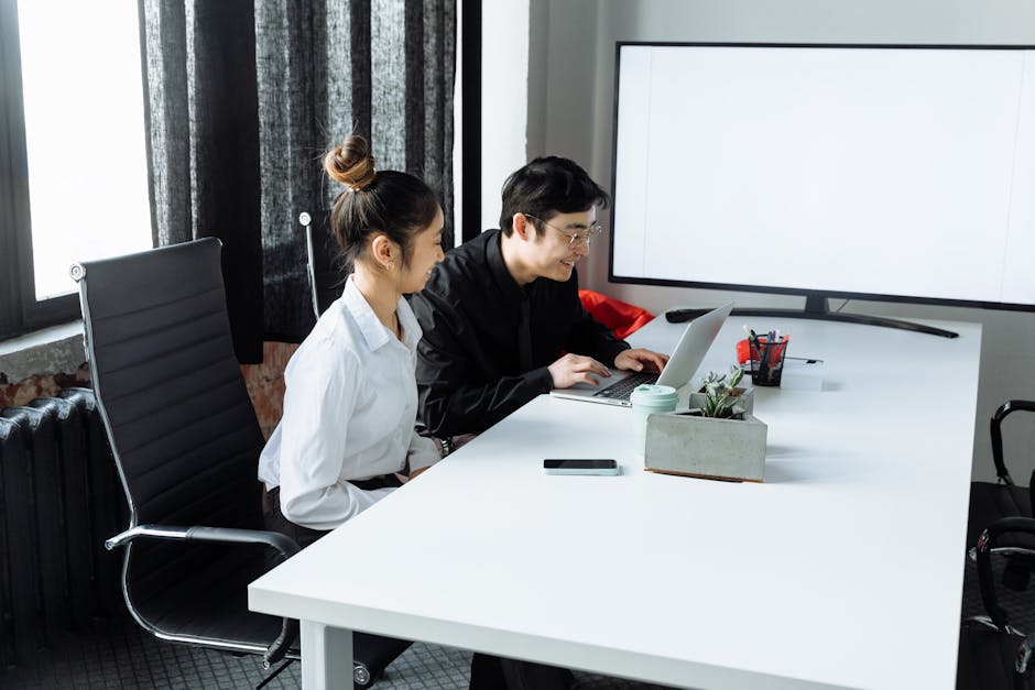 A professional woman smiling as she works on a project on her laptop in a bright, modern office.